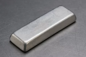 تصویر یک شمش فلز کادمیوم با سطح نقره‌ای و براق روی زمینه‌ای فلزی خاکستری؛ نمای نزدیک از بافت و رنگ واقعی این فلز سنگین صنعتی. 