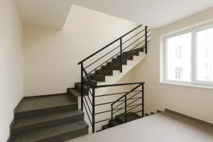 باکس راه‌پله مدرن با نرده فلزی مشکی، پله‌های سنگی تیره و نور طبیعی از پنجره بزرگ، مطابق ضوابط طراحی پله در ساختمان» 