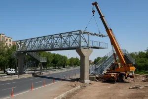 عملیات نصب پل عابر پیاده فلزی بر روی خیابان شهری با استفاده از جرثقیل در روز روشن
