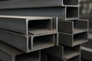 تیرآهن‌های فولادی خاکستری چیده‌شده در انبار صنعتی، با جزئیات واضح از سطح فلز و بافت طبیعی فولاد بدون زنگ‌زدگی.
