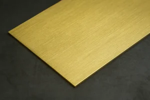 ورق لاتون طلایی براق روی سطح تیره فلزی، بافت برس‌خورده و سطح صیقلی