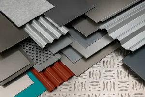  تصویر واقعی از انواع ورق‌های ساختمانی شامل ورق گالوانیزه، ورق رنگی، ورق استیل، ورق آلومینیوم و ورق‌های طرح‌دار که به‌صورت لایه‌ای روی هم چیده شده‌اند و تنوع رنگ و بافت آن‌ها نشان داده شده است.
