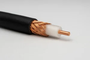 نمای نزدیک از کابل کواکسیال بریده‌شده که لایه‌های داخلی آن شامل رسانای مسی مرکزی، عایق سفید، شیلد بافته‌شده مسی و روکش بیرونی مشکی مشخص است؛ روی پس‌زمینه روشن و بدون نوشته.
