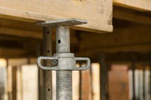  نمای نزدیک از سرجک قالب‌بندی فلزی در کارگاه ساختمانی که برای نگهداری قالب‌های چوبی در عملیات بتن‌ریزی استفاده می‌شود.
