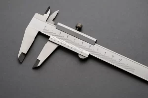 تصویر نزدیک از کولیس ورنیه استیل روی سطح خاکستری.
