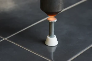  عملیات نصب و جوش گل‌میخ فلزی روی سطح سرامیکی تیره با استفاده از دستگاه جوشکاری مخصوص در محیط کارگاهی 