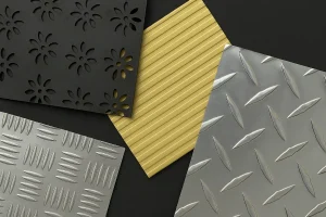 تصویر چند نمونه ورق فلزی طرح‌دار شامل ورق مشکی گلدار، ورق طلایی شیاردار، و ورق نقره‌ای آج‌دار و الماسی که روی سطح تیره چیده شده‌اند و بافت و درخشش فلزها را نشان می‌دهد.
